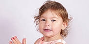 Mya a rejoint le concours — aidez-le/la à gagner de superbes lots ! toddler, child, clapping, curly_hair, smiling, portrait, dress, peach_color, face, hands, cute, happy, studio, light_background, young_child, skin, expression, innocent, closeup, person