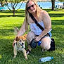 woman, dog, grass, tree, lake, outdoor, sunny, leash, water_bottle, dog_bowl, sunglasses, casual_clothing, smiling, nature, park, summer, pet, recreation, people, shade