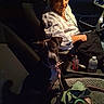 dog, puppy, person, car_interior, seat, night, woman, leash, bottle, handbag, blanket, toy, seatbelt, window, dashboard, clothing, face, pet, restraint, container