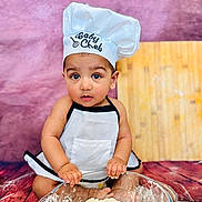 Aalam joined the competition — help win amazing prizes! apron, baby, chef_hat, child, cooking, cute, expression, floor, flour, food_preparation, glass_bowl, hands, indoors, kitchen, playful, portrait, purple_background, sitting, small_child, wooden_floor