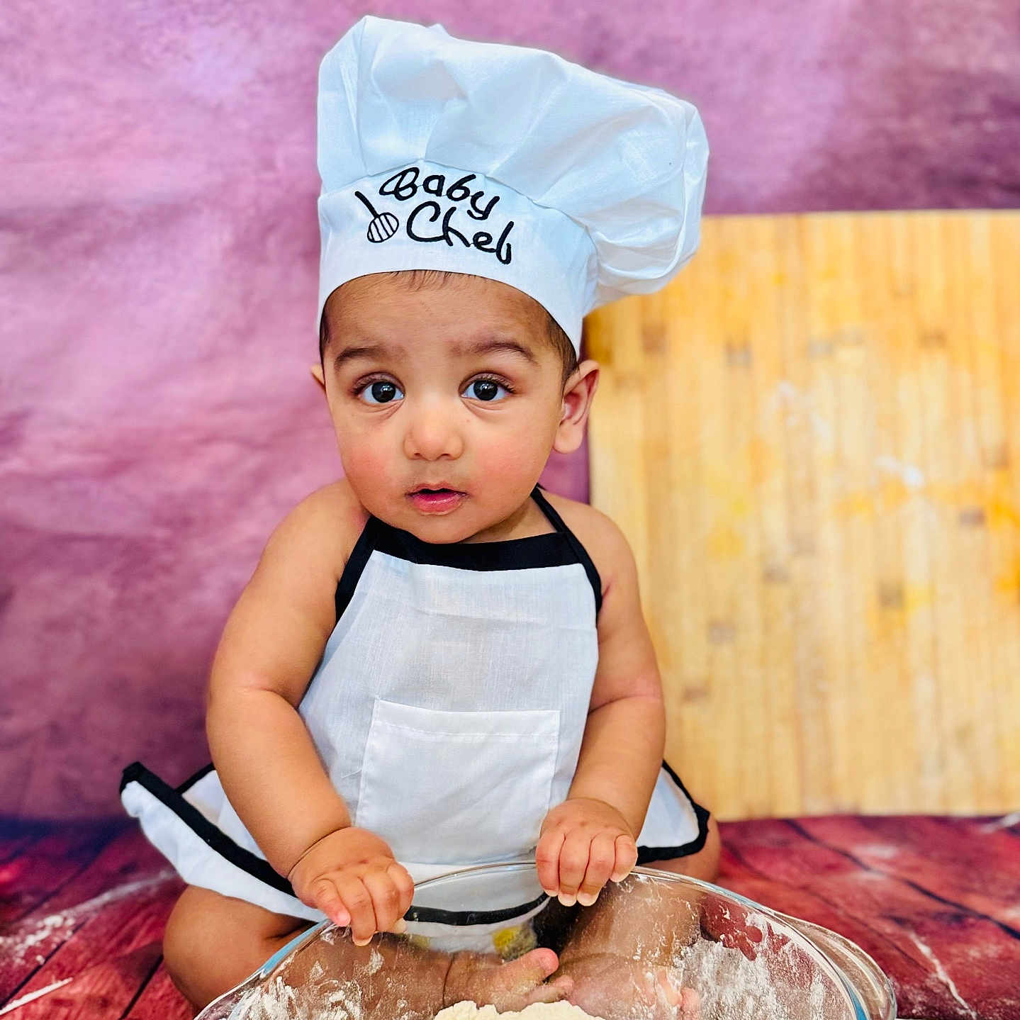 Aalam joined the competition — help win amazing prizes! apron, baby, chef_hat, child, cooking, cute, expression, floor, flour, food_preparation, glass_bowl, hands, indoors, kitchen, playful, portrait, purple_background, sitting, small_child, wooden_floor