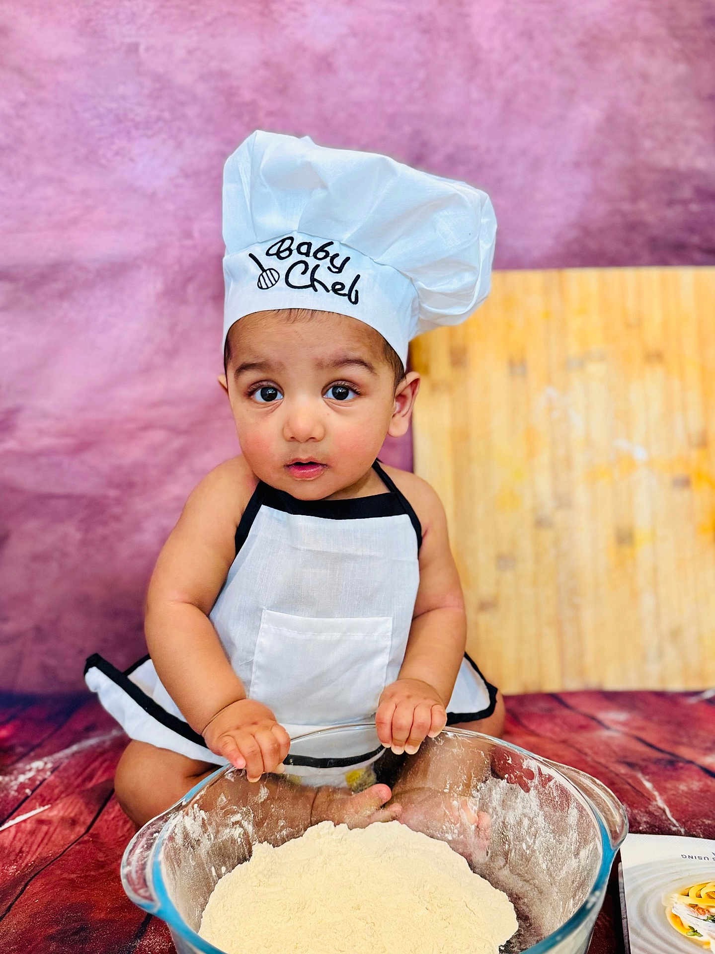 Aalam joined the competition — help win amazing prizes! apron, baby, chef_hat, child, cooking, cute, expression, floor, flour, food_preparation, glass_bowl, hands, indoors, kitchen, playful, portrait, purple_background, sitting, small_child, wooden_floor