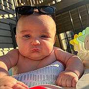 Kaine is registered to the contest to win money with this photo: baby, child, sunglasses, toy, hand, face, outdoor, sunlight, expression, pout, plastic, star_toy, table, arm, infant, person, closeup, skin, play, summer