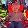 Hudson is registered to the contest to win money with this photo: child, toddler, baby, portrait, smiling, outdoor, seated, wagon, stroller, red, sweater, jeans, blond_hair, sunlight, garden, lawn, family, adults, house, play_equipment