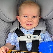 Hudson is registered to the contest to win money with this photo: baby, child, infant, smiling, car_seat, seatbelt, harness, vehicle, car_interior, toy, remote_control, sippy_cup, blue_cup, blond_hair, portrait, indoors, travel, safe_seating, red_car, happy