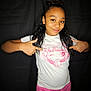 child, girl, smiling, white_tshirt, anime_print, pink_pants, pointing, portrait, black_background, casual_clothing, youth, happy, standing, long_hair, fashion, cute, playful, expression, indoor, person