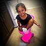 child, girl, smiling, curly_hair, black_shirt, pink_stroller, toy, indoor, floor, kitchen, shoes, playful, happy, young_child, person, cute, sitting, small_toy, colorful, home