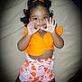 Aluna is registered to the contest to win money with this photo: child, toddler, curly_hair, orange_top, patterned_shorts, peach_print, bow, lying_down, beige_background, hands_up, cute, playful, smiling, portrait, indoor, clothing, person, baby, happy, skin