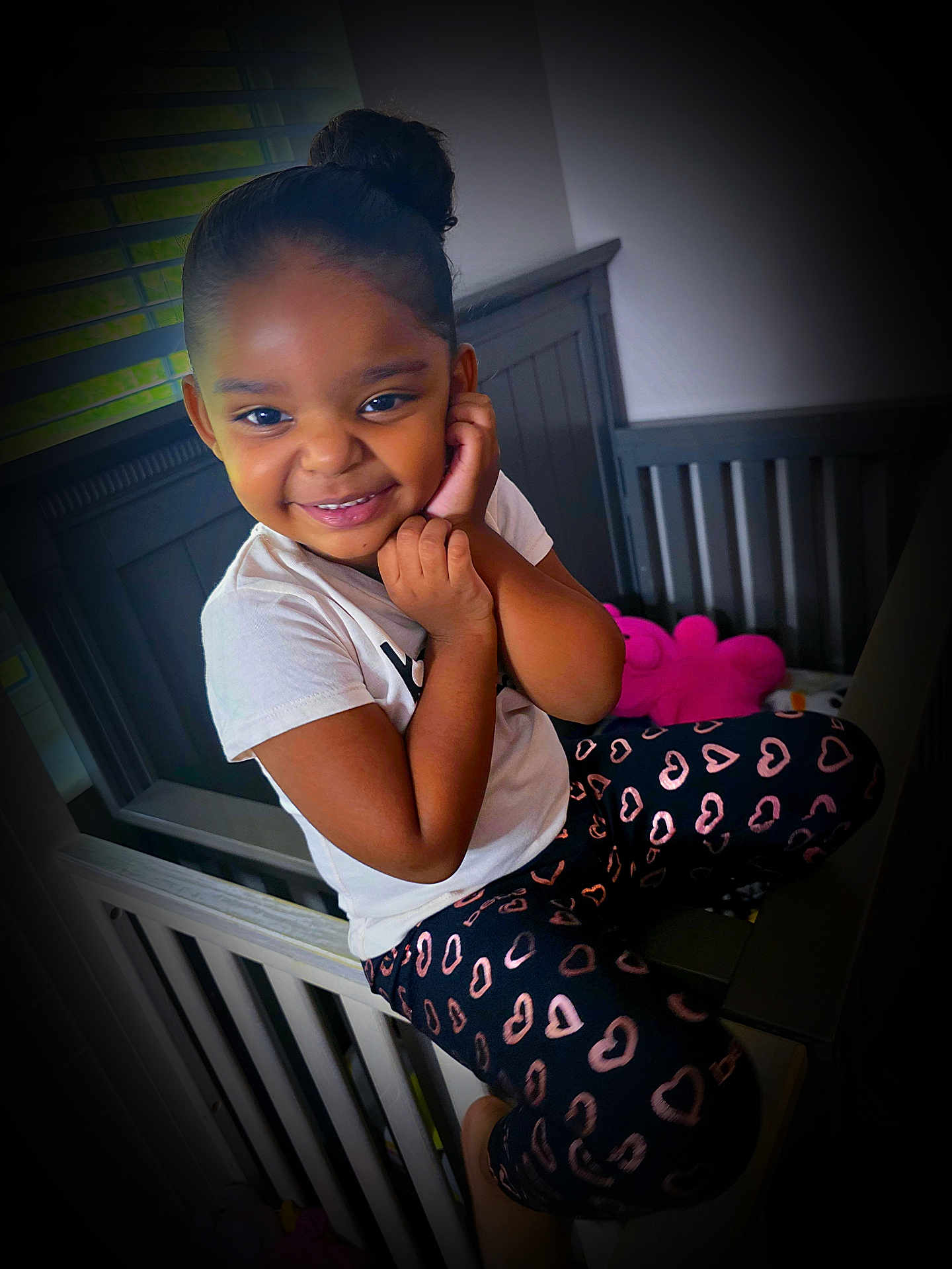 Aluna joined the competition — help win amazing prizes! child, girl, smiling, crib, nursery, plush_toy, heart_pattern, leggings, white_tshirt, hair_bun, indoor, playful, cute, happy, childhood, furniture, window_blinds, home, portrait, seated