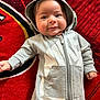 Santiago is registered to the contest to win money with this photo: baby, infant, hoodie, gray_clothing, nike, onesie, carpet, red_carpet, smile, face, cute, child, indoors, portrait, lying_down, young_child, happy, casual_clothing, zipper, hand