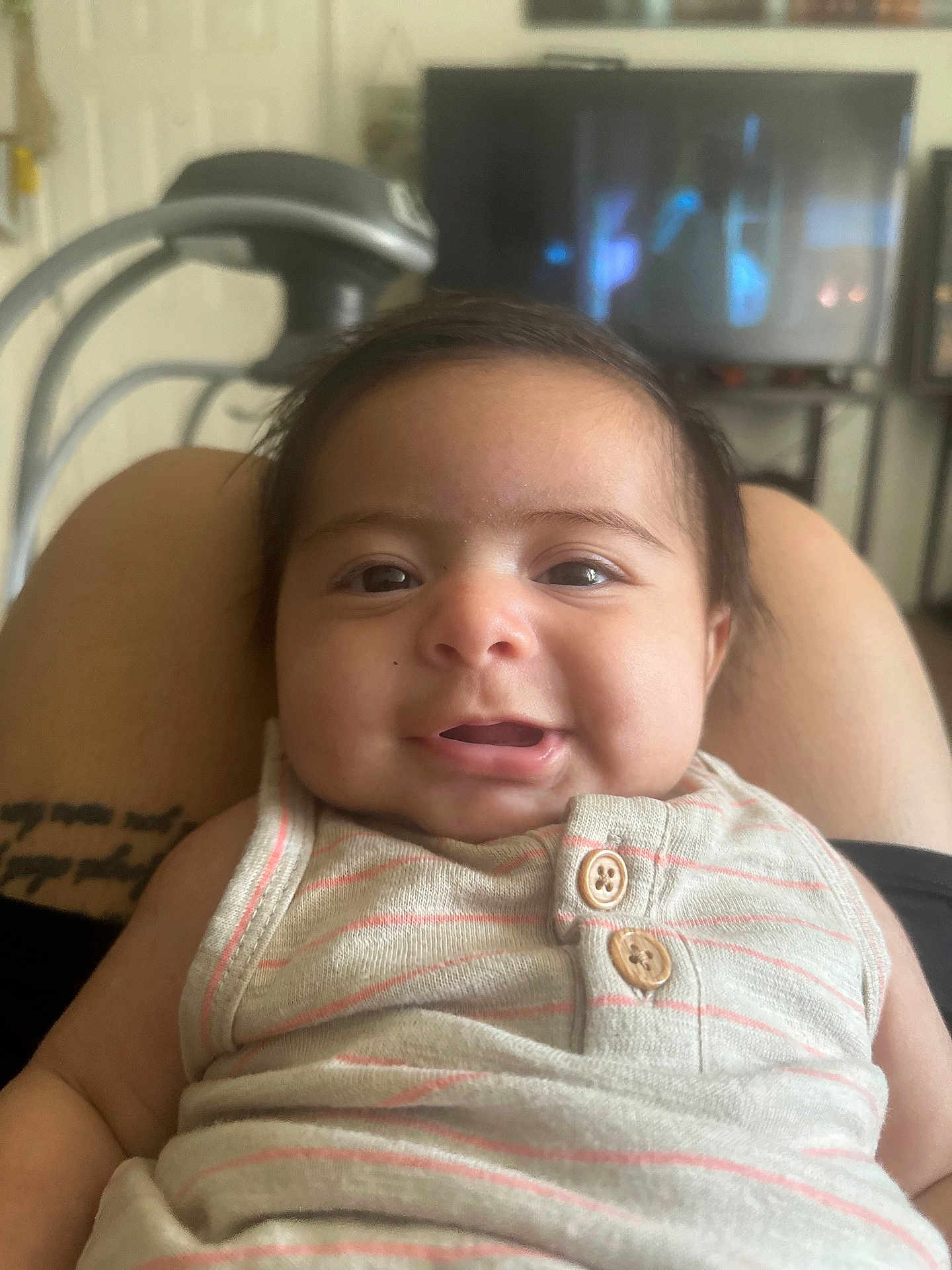 Santiago is registered to the contest to win money with this photo: baby, smiling, person, face, indoor, clothing, striped, button, lap, furniture, television, exercise_equipment, skin, head, happy, child, infant, portrait, casual, relaxed