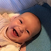 Rose is registered to the contest to win money with this photo: baby, smiling, face, infant, knitted_blanket, cozy, pastel_colors, happy, cute, child, portrait, soft_lighting, warm, lying_down, person, indoors, closeup, skin, head, expression