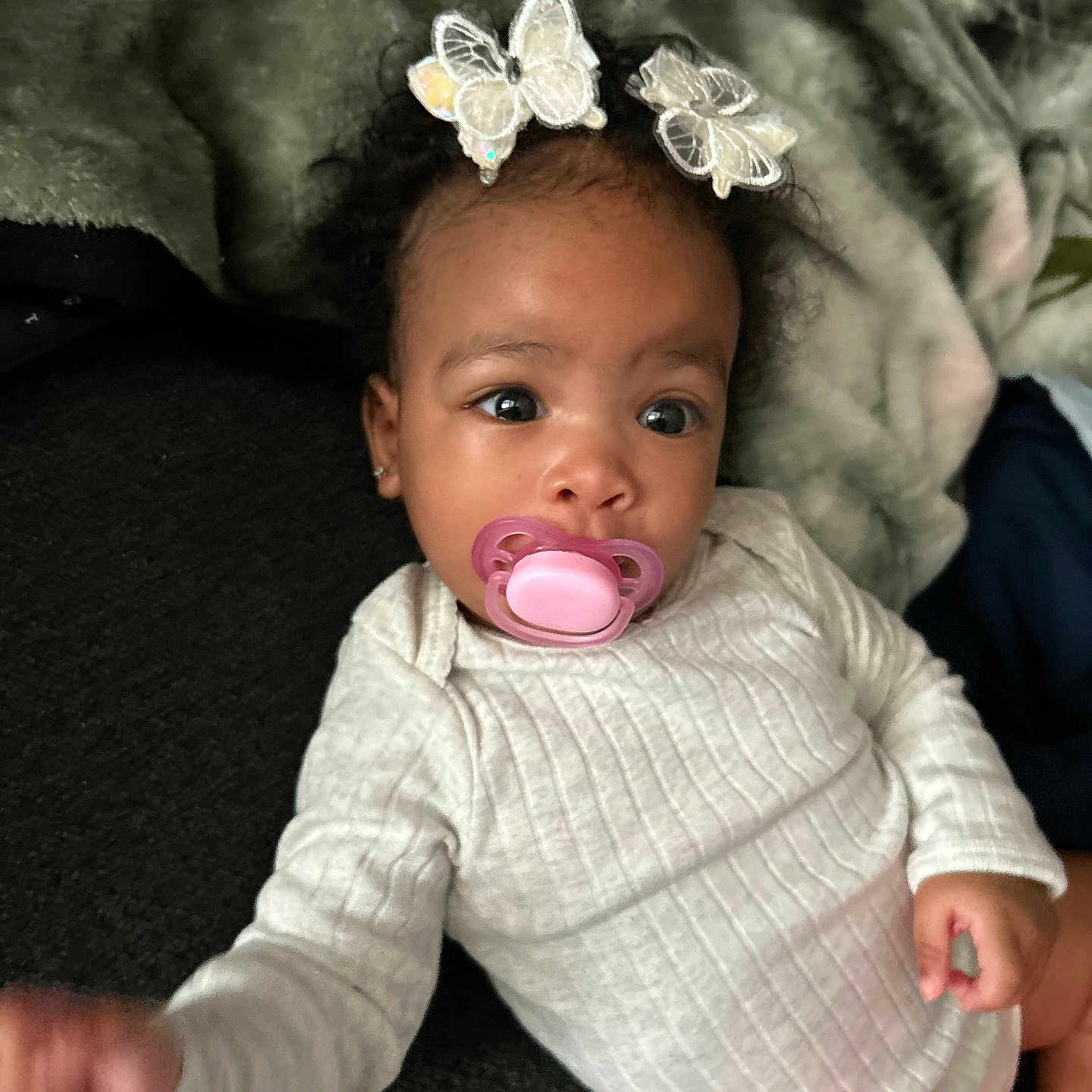 Alyce joined the competition — help win amazing prizes! baby, blanket, butterfly_clips, child, cozy, curious, cute, face, hair_accessory, hand, head, indoors, infant, lying_down, pacifier, portrait, skin, soft, white_clothing, young