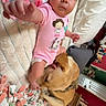 Vivianna is registered to the contest to win money with this photo: baby, infant, dog, bed, blanket, pink_onesie, reaching_hand, indoor, furniture, television, room, person, animal, pet, wooden_drawer, floral_pattern, couch, curly_hair, skin, home