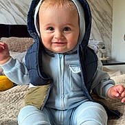 Maxson joined the competition — help win amazing prizes! baby, child, smiling, hoodie, vest, sitting, indoor, blanket, soft_texture, cute, happy, person, infant, clothing, feet, sock, face, portrait, home, cozy