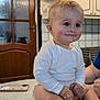 Maxson is registered to the contest to win money with this photo: arm, baby, cabinet, child, closeup, counter, cute, domestic, face, happy, indoors, infant, kitchen, person, sitting, smiling, table, tile_wall, white_onesie, wooden_door