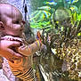 aquarium, baby, child, colorful, coral, curious, exploration, fish, glass, hand, indoor, marine_life, person, reflection, rock, smile, striped_clothing, supporting_hand, underwater_life, water
