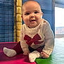 baby, child, clothing, cute, daylight, floor, happy, indoor, infant, netting, padded_mat, person, play_area, portrait, red_bow, sitting, smiling, sock, sweater, window