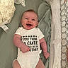 baby, infant, smile, onesie, crib, mesh, bedding, happy, child, cute, lying_down, clothing, person, indoors, text_on_clothing, fabric, soft, skin, head, arm