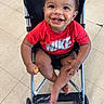 toddler, child, stroller, smile, red_shirt, nike, happy, indoor, floor, tile, baby, sitting, snack, food, cute, playful, feet, hands, person, casual
