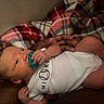 Kamari joined the competition — help win amazing prizes! baby, newborn, pacifier, onesie, nike, baseball, plaid_blanket, hand, arm, skin, infant, clothing, resting, indoor, curious, person, portrait, child, soft_texture, cozy