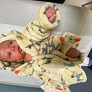 Kamari is registered to the contest to win money with this photo: baby, infant, robe, blanket, animal_print, medical_table, baby_wipes, hand, phone, curious, lying_down, newborn, clothing, soft_texture, indoor, person, skin, cute, child, hospital