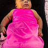 baby, sleeping, pink_clothing, black_cushion, purple_background, infant, child, peaceful, resting, portrait, young_child, indoors, cute, relaxed, blanket, soft_texture, head, face, small_hands, cozy