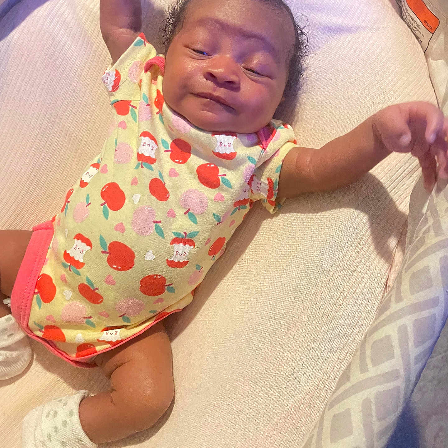 Icelynn joined the competition — help win amazing prizes! baby, infant, child, onesie, apple_pattern, cushion, sleepy, cute, lying_down, soft_surface, sock, arm_stretch, content, indoor, fabric, pattern, head, skin, person, newborn