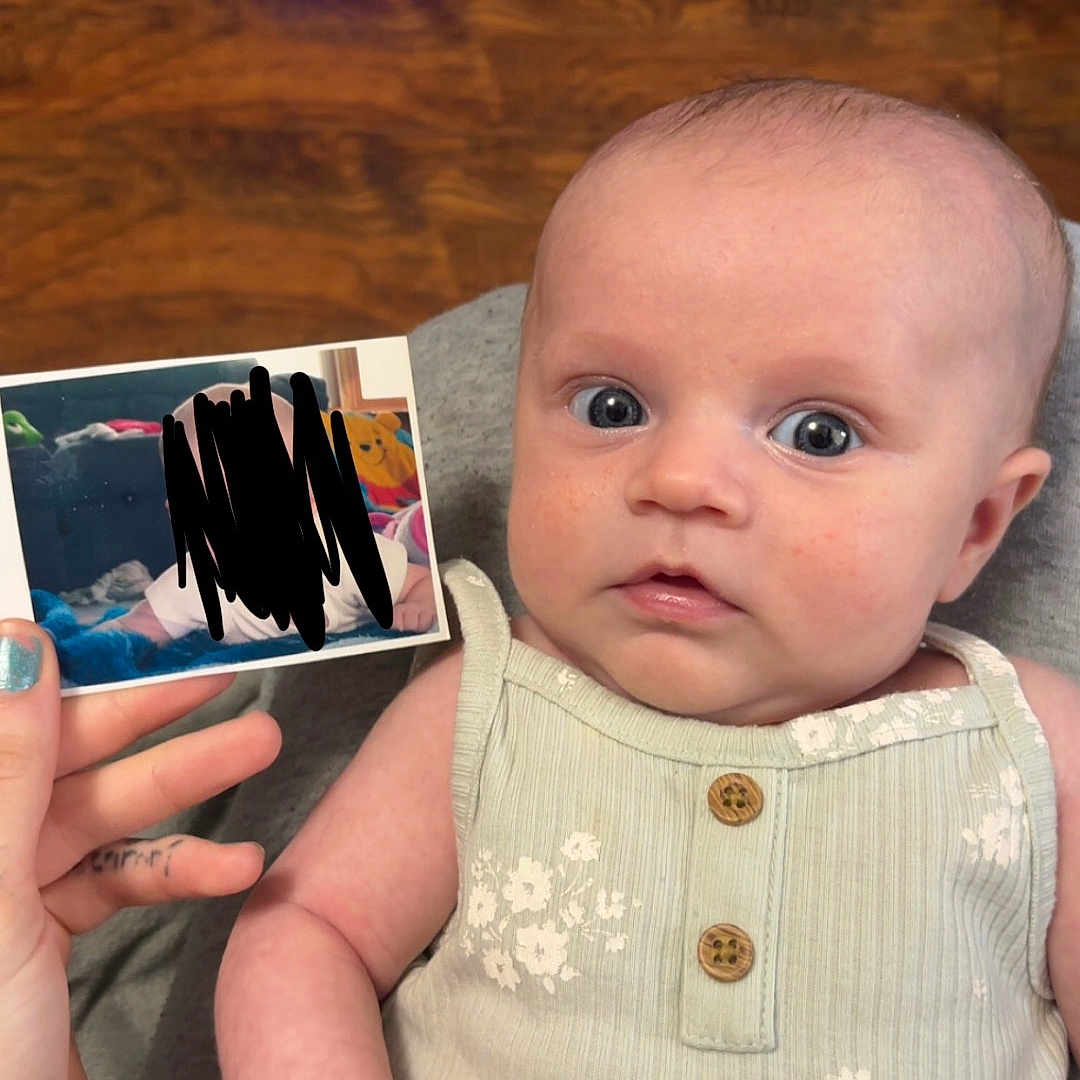 Heidi Lynn joined the competition — help win amazing prizes! baby, infant, face, eyes, hand, onesie, clothing, photo, wood_floor, indoor, person, skin, fingernails, expression, sitting, holding, young_child, portrait, cute, curious