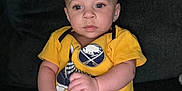 Gianni is registered to the contest to win money with this photo: baby, child, infant, yellow_onesie, sitting, portrait, face, eyes, hands, legs, indoor, cute, expression, clothing, person, young, skin, hair, background, couch