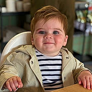 Louis is registered to the contest to win money with this photo: toddler, child, high_chair, striped_shirt, beige_jacket, smile, face, table, indoor, person, cute, rosy_cheeks, eyes, hand, clothing, portrait, baby, happy, furniture, seated