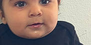 Lucas is registered to the contest to win money with this photo: baby, child, face, eyes, black_clothing, gold_design, portrait, closeup, curious, indoor, young, infant, cute, chubby_cheeks, person, head, expression, skin, hair, sitting