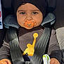 baby, child, pacifier, car_seat, seatbelt, beanie, black_clothing, gold_logo, hand, toy, infant, straps, closeup, portrait, serious_expression, indoors, safety, cute, person, headwear