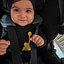 baby, child, car_seat, smile, hat, black_clothing, gold_logo, straps, hands, close_up, infant, cute, seatbelt, portrait, indoors, face, happy, young_child, person, casual