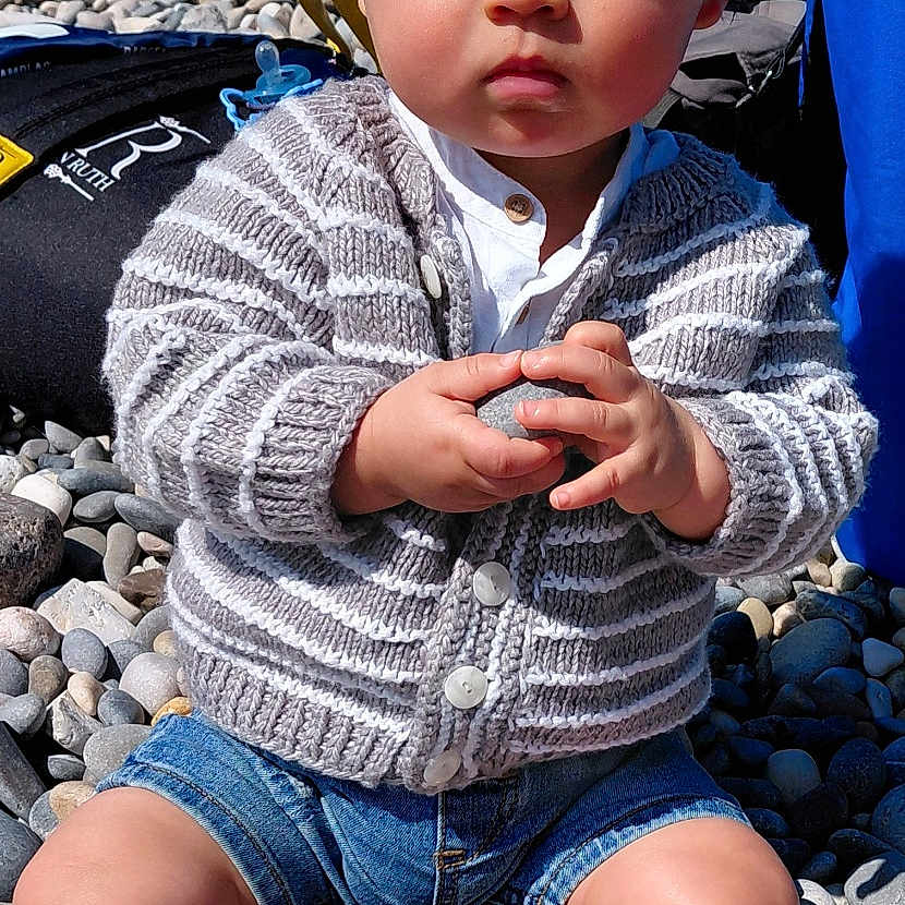 Bruno participe au concours pour gagner de l'argent avec cette photo : toddler, child, outdoor, pebbles, rock, sweater, denim_shorts, black_sneakers, serious_expression, sunny, sky, trees, baby, sitting, holding, casual_clothing, nature, portrait, daytime, young_child