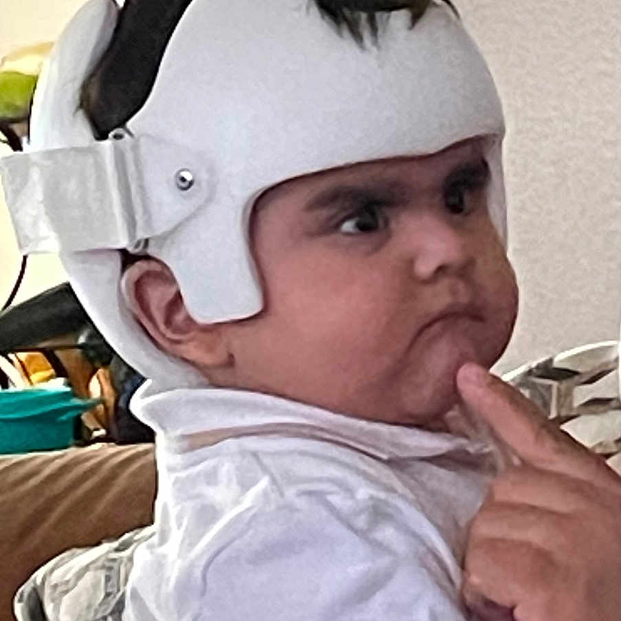 Jose is registered to the contest to win money with this photo: baby, casual, child, couch, expression, face, furniture, hand, helmet, home, indoor, people, person, portrait, seated, short_hair, thinking, thoughtful, white_clothing, young