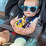 baby, child, car_seat, sunglasses, toy, blue_sunglasses, car_interior, child_safety, seatbelt, infant, person, tattoo, adult, clothing, summer_outfit, window, light, seat, portrait, cute