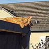 cat, ginger_cat, animal, pet, outdoor, sunlight, roof, building, canopy, paw, relaxing, daytime, sky, house, window, plant, leaf, shade, resting, feline
