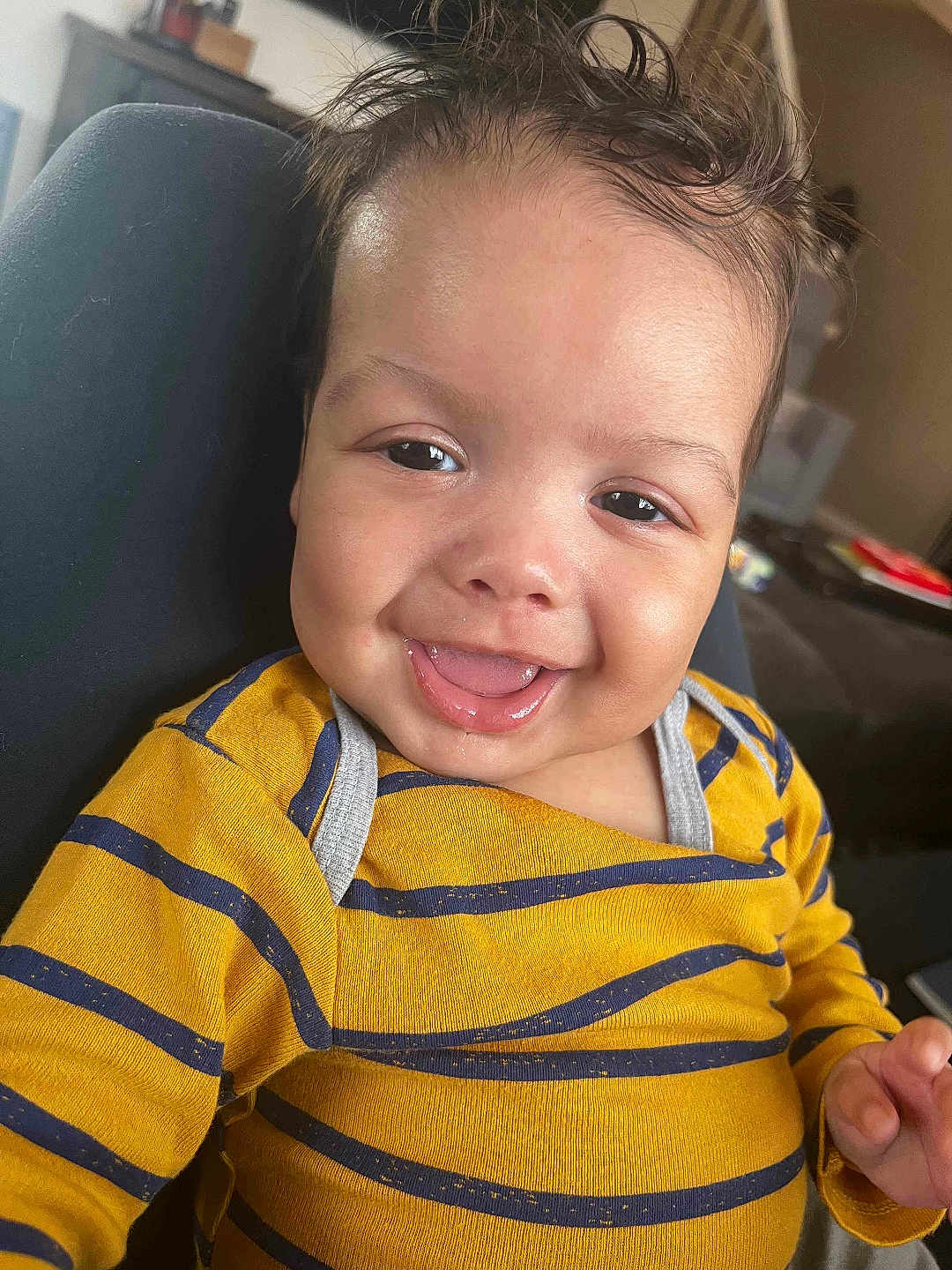 Ellias is registered to the contest to win money with this photo: baby, infant, smile, drooling, tongue_out, striped_shirt, yellow_shirt, close_up, face, eyes, hair, cheeks, seat, couch, indoor, portrait, happy, cute, child, onesie