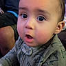 Tre'Von Gibbons Jr is registered to the contest to win money with this photo: baby, child, indoor, person, curious, dinosaur_pattern, onesie, tousled_hair, wide_eyes, expression, cozy, warm_lighting, blurred_background, adult, seated, closeup, portrait, hand, face, infant
