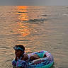 Mya participe au concours pour gagner de l'argent avec cette photo : child, goggles, floaties, inflatable_ring, water, ocean, sunset, reflection, beach, swimming, playful, summer, outdoor, vacation, fun, waves, sky, sun, relaxation, holiday