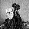 man, dog, older_adult, glasses, black_and_white, portrait, indoor, couch, pet, animal, seated, shoulder, wall, frame, pattern, looking_at_camera, casual, companion, friendship, home
