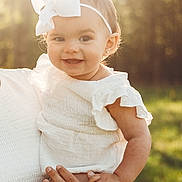 Kennedy joined the competition — help win amazing prizes! baby, child, smiling, white_bow, headband, outdoor, sunlight, nature, greenery, portrait, happy, infant, holding, adult_hand, white_clothing, cute, earrings, warm_light, person, closeup