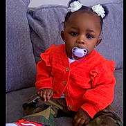 Nevaeha joined the competition — help win amazing prizes! toddler, child, pacifier, orange_sweater, camouflage_pants, red_shoes, flower_hair_accessories, couch, gray_couch, indoors, cute, sitting, young_child, baby, fashion, portrait, casual_clothing, cozy, home, person