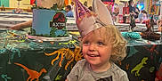Axton joined the competition — help win amazing prizes! balloon, bench, birthday_party, cake, celebration, child, clothing, curly_hair, decoration, dinosaur, event, festive, fun, happy, indoor, party_hat, person, smile, table, toddler