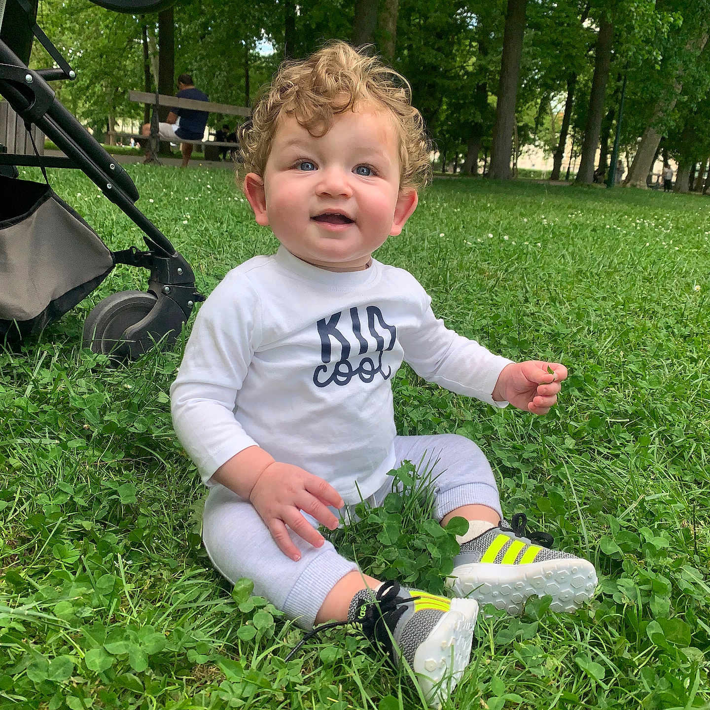 Laouni participe au concours pour gagner de l'argent avec cette photo : casual_clothing, child, clover, curly_hair, cute, daylight, grass, greenery, happy, nature, outdoor, park, person, playful, relaxation, sitting, smiling, sneakers, stroller, toddler