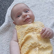 Frankie is registered to the contest to win money with this photo: baby, smiling, yellow_outfit, towel, carpet, infant, face, hand, cute, lying_down, indoors, child, portrait, soft_texture, buttoned_clothing, happy, skin, expression, small_fingers, casual
