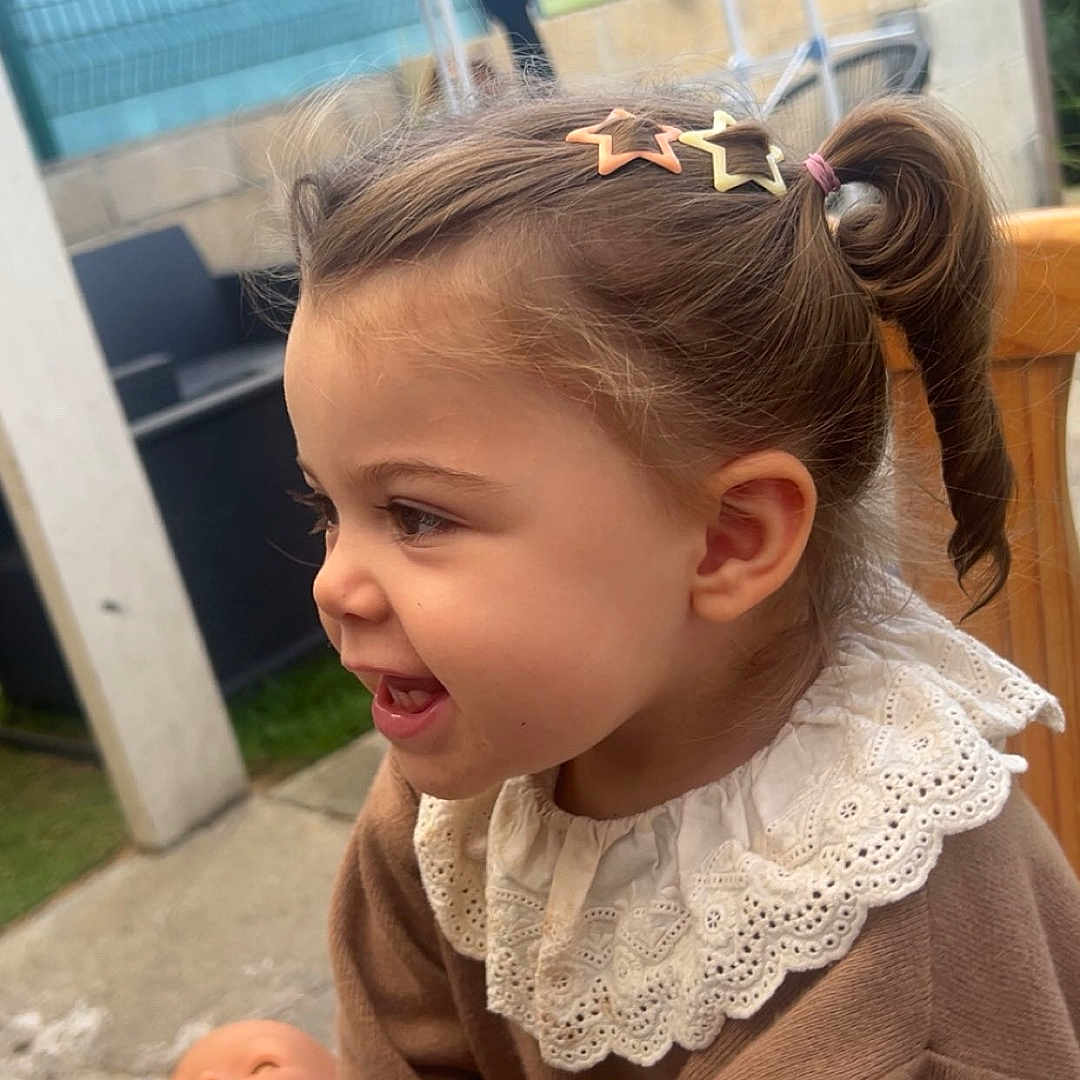 Chiara participe au concours pour gagner de l'argent avec cette photo : backyard, casual, child, clothing, cute, daylight, doll, hair_clip, happy, lace_collar, outdoor, person, play, pony_tail, portrait, seated, smiling, toddler, toy, young_child