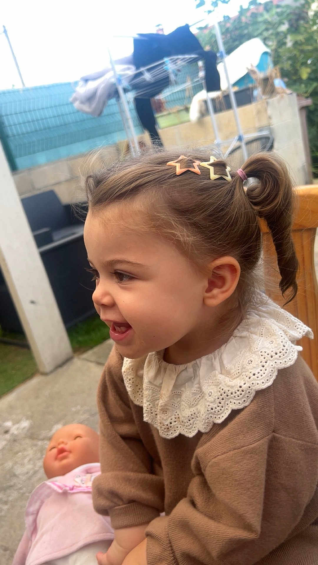 Chiara participe au concours pour gagner de l'argent avec cette photo : toddler, child, smiling, hair_clip, pony_tail, doll, outdoor, backyard, clothing, lace_collar, happy, cute, person, young_child, play, toy, portrait, casual, seated, daylight