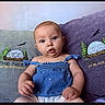 Anya is registered to the contest to win money with this photo: baby, child, infant, blue_top, pillow, embroidery, sitting, indoors, cute, curious, face, person, young, portrait, comfortable, expression, hands, cushion, background, clothing